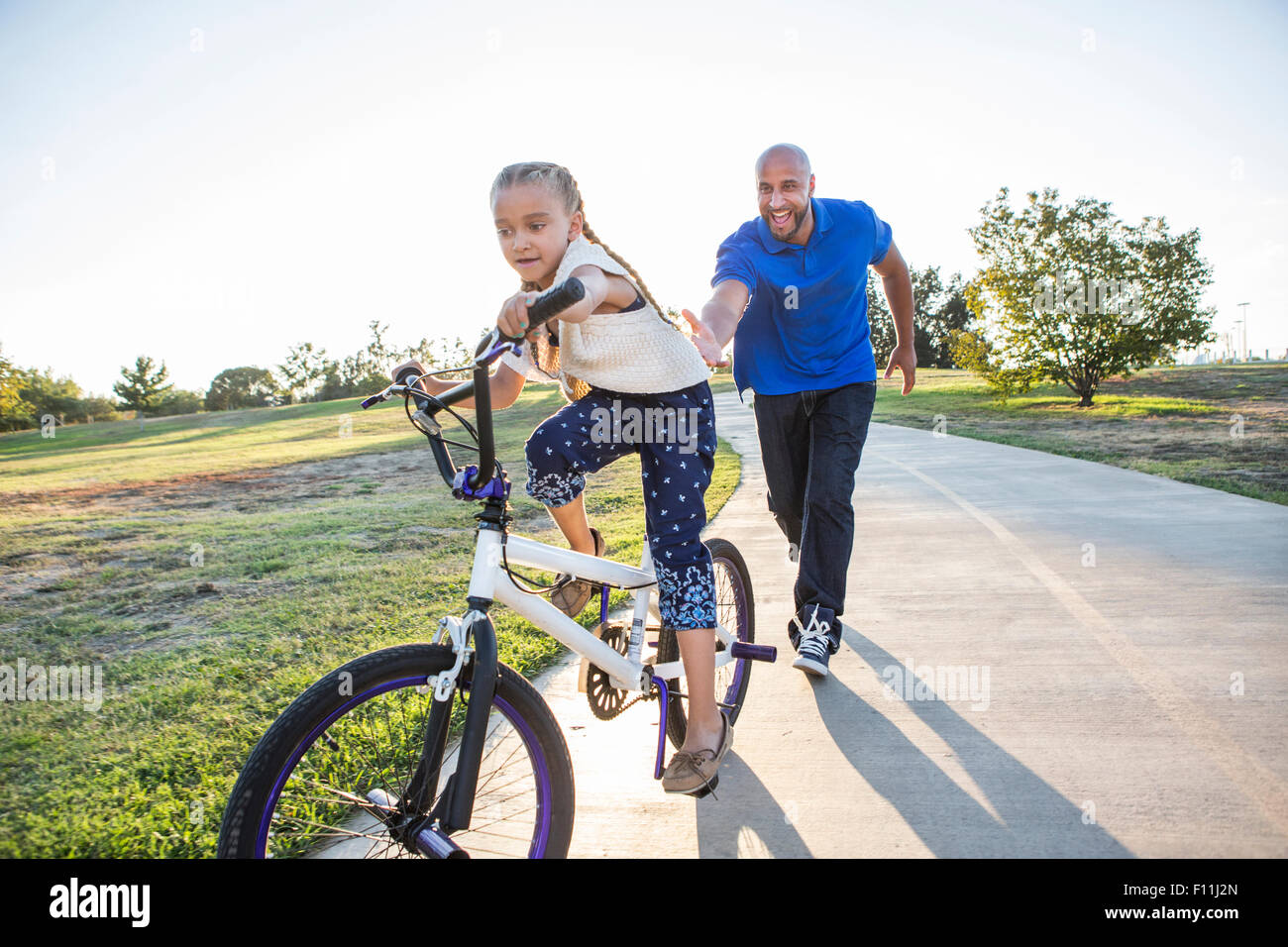 Father teaching daughter to ride bicycle in park Stock Photo