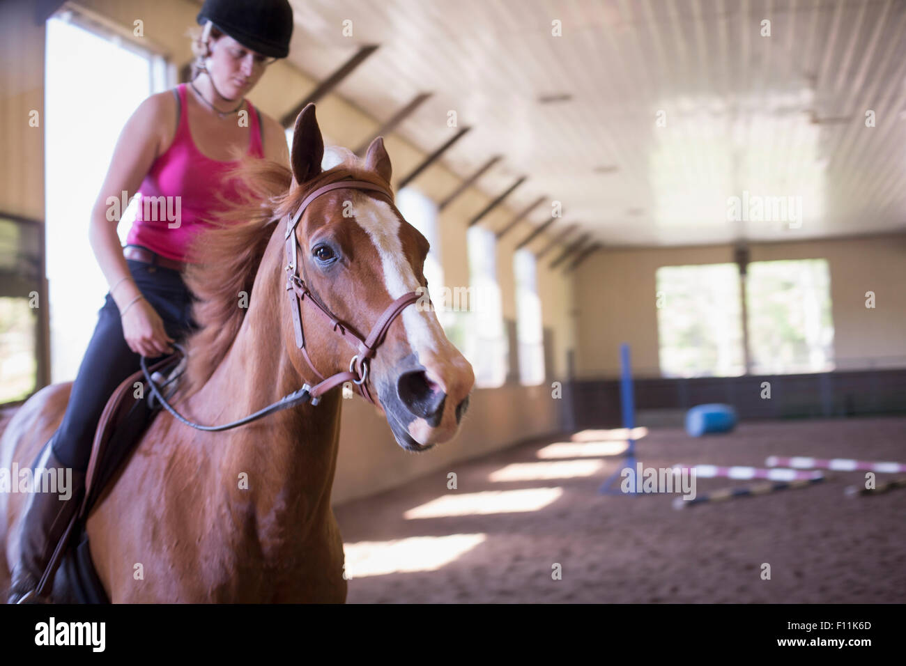 Caucasian woman riding horse in indoor paddock Stock Photo