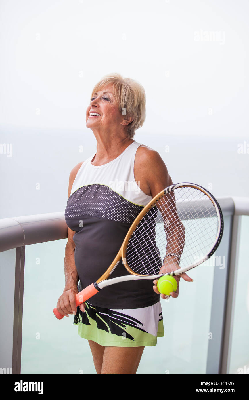 Older Caucasian woman holding tennis racket on balcony Stock Photo