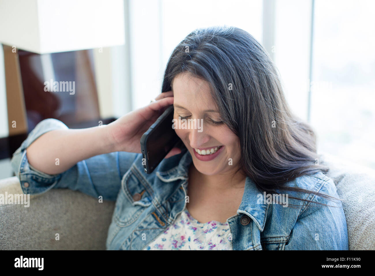 Hispanic woman talking on cell phone on sofa Stock Photo