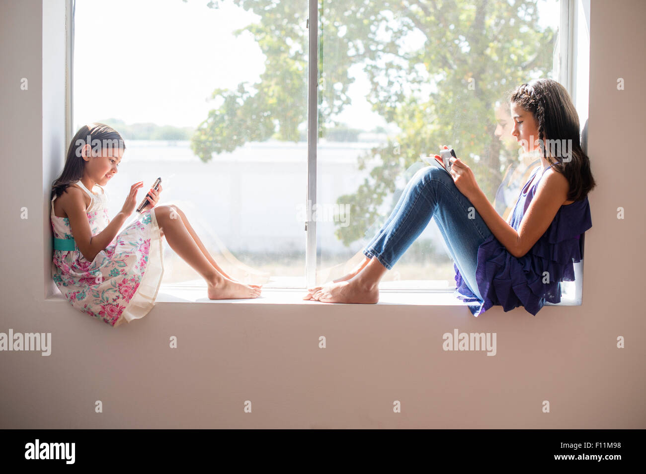 Sisters using technology in window Stock Photo - Alamy