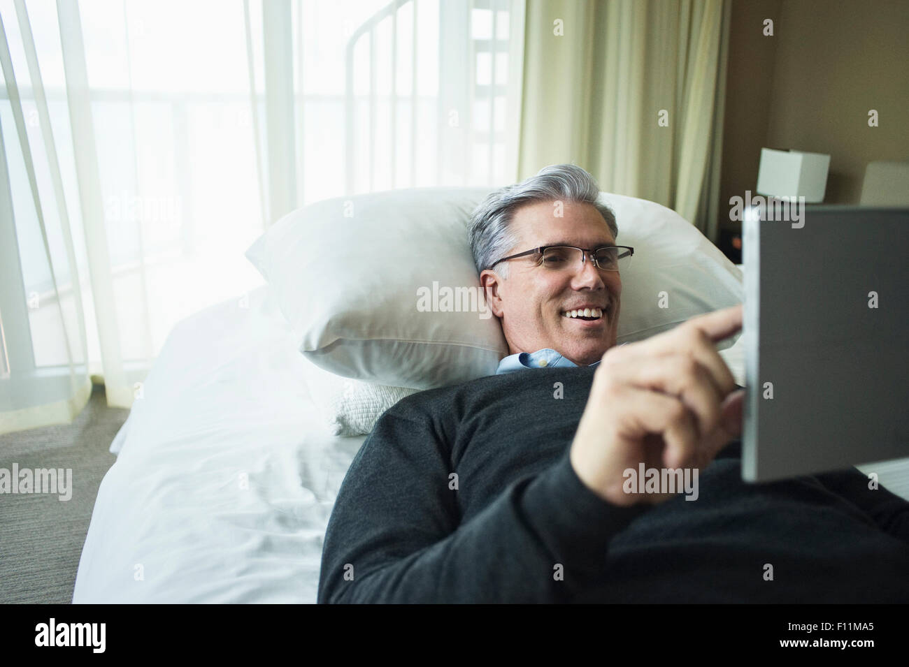 Caucasian man using digital tablet in bed Stock Photo