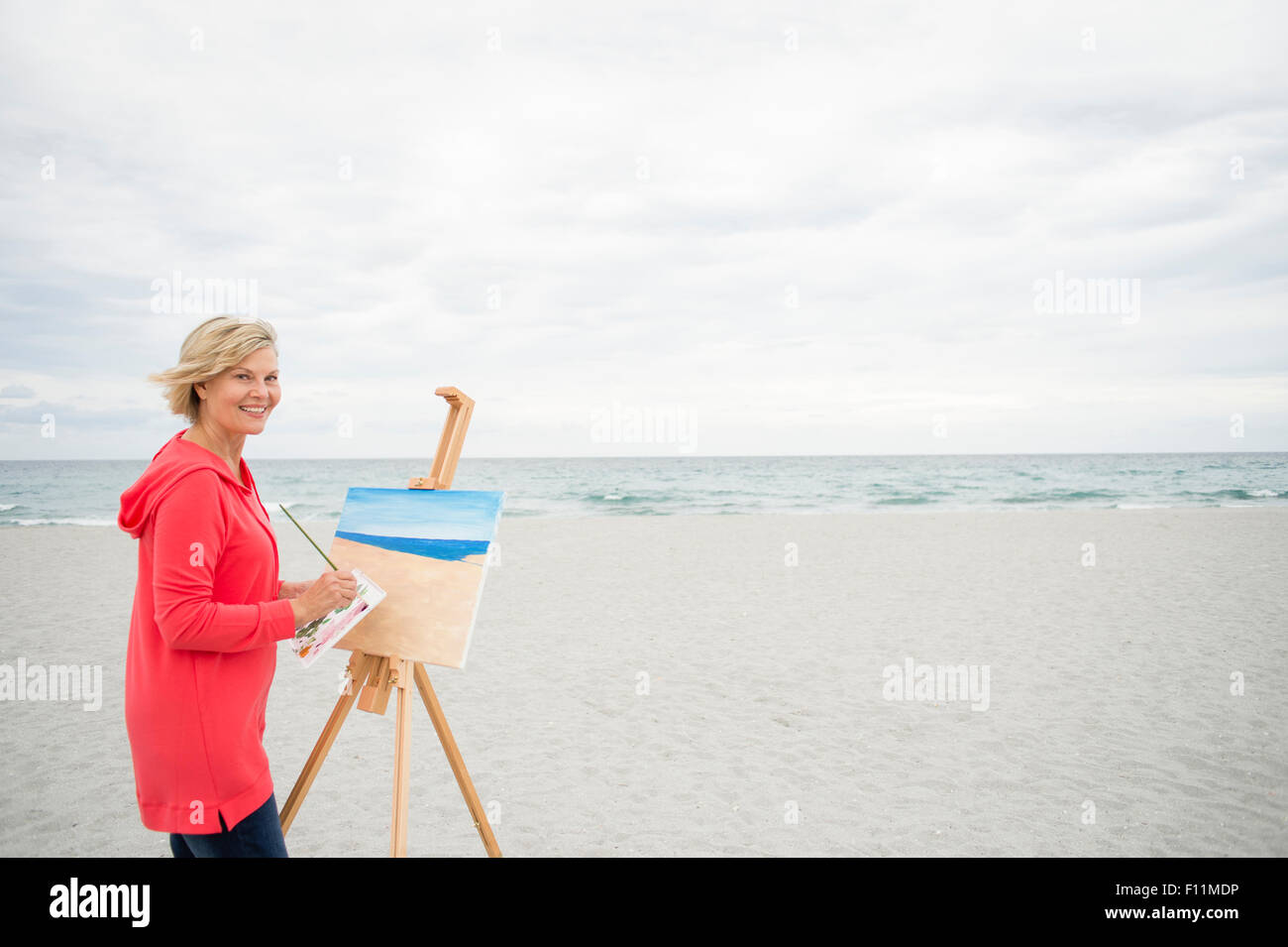 Older Caucasian woman painting on beach Stock Photo