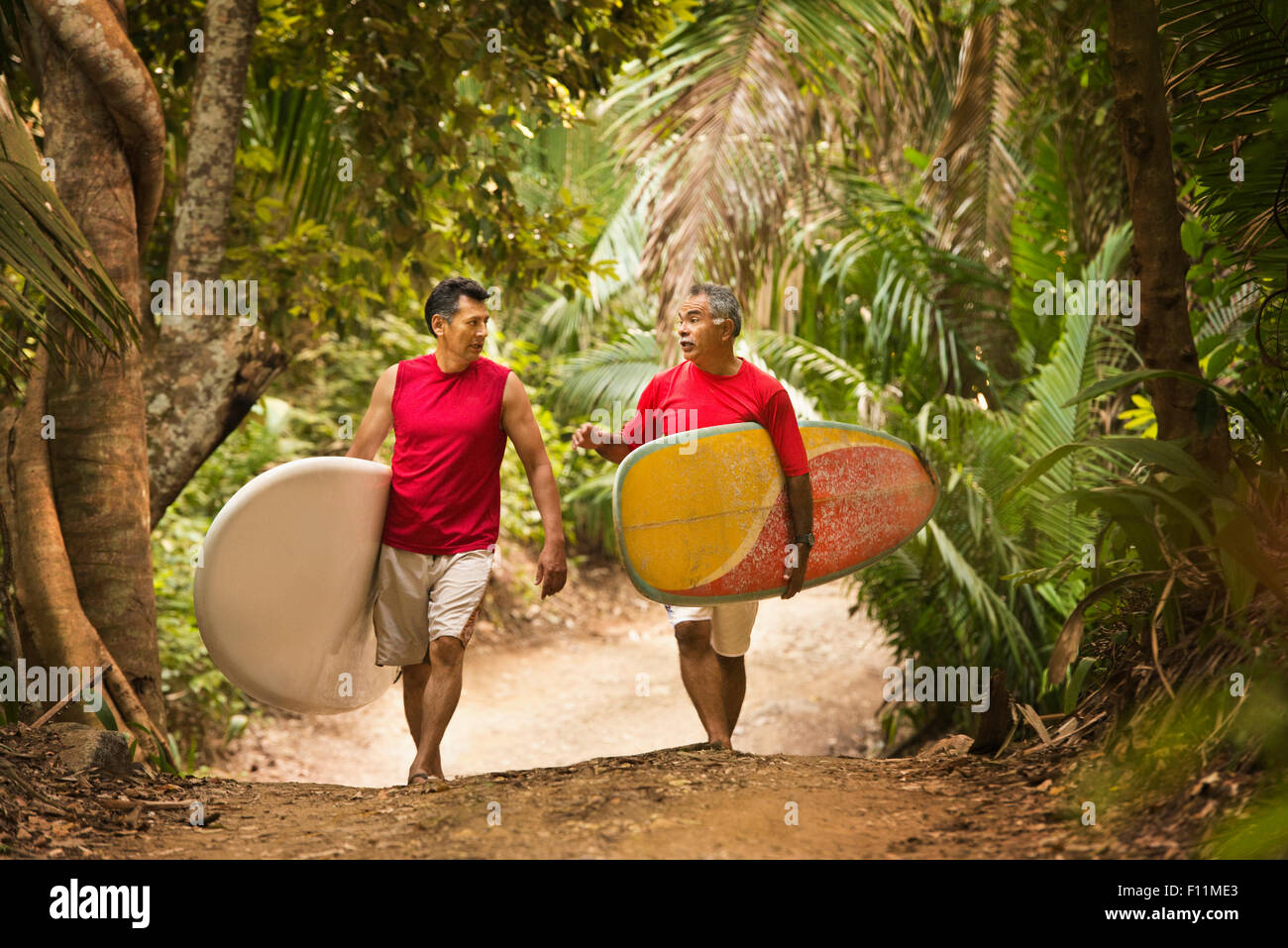 Hispanic men carrying surfboards on jungle trail Stock Photo