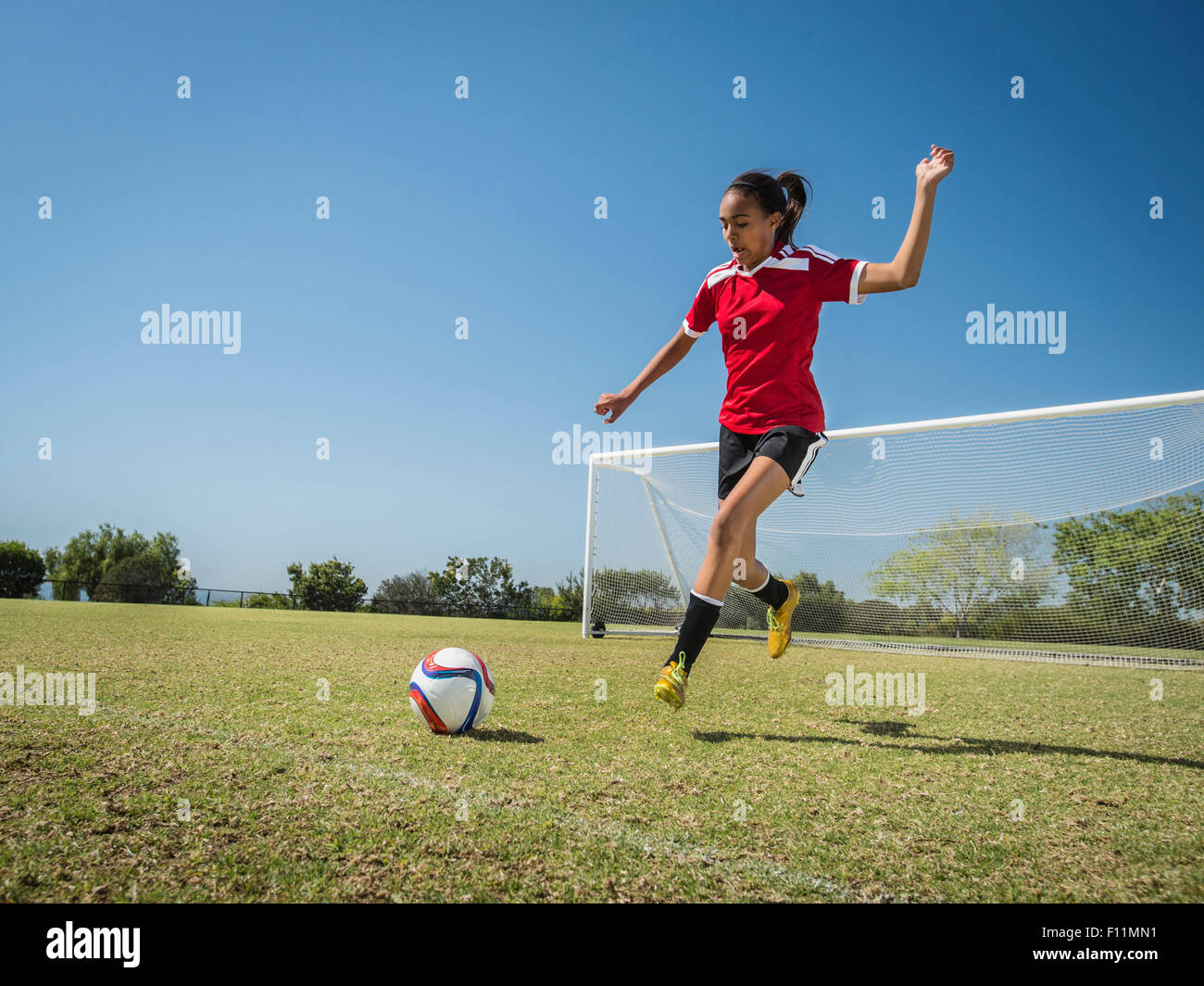 Mixed race soccer player kicking ball on field Stock Photo