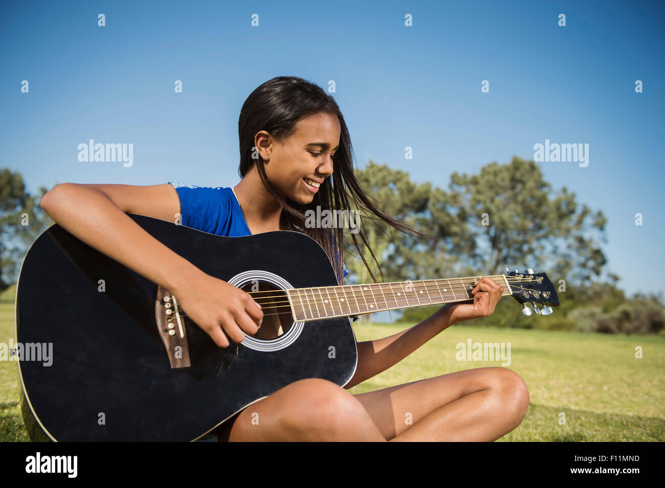 Mixed race girl playing guitar in park Stock Photo
