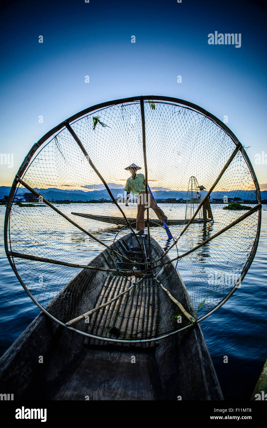 Asian fisherman using fishing net in canoe on river Stock Photo