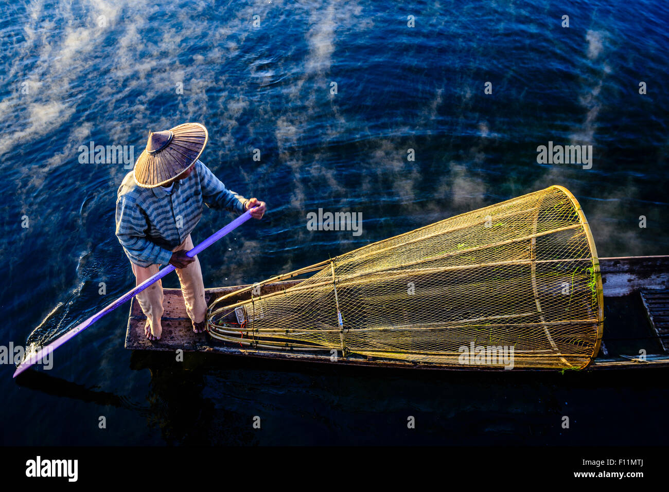 High angle view of Asian fisherman using fishing net in canoe on river Stock Photo