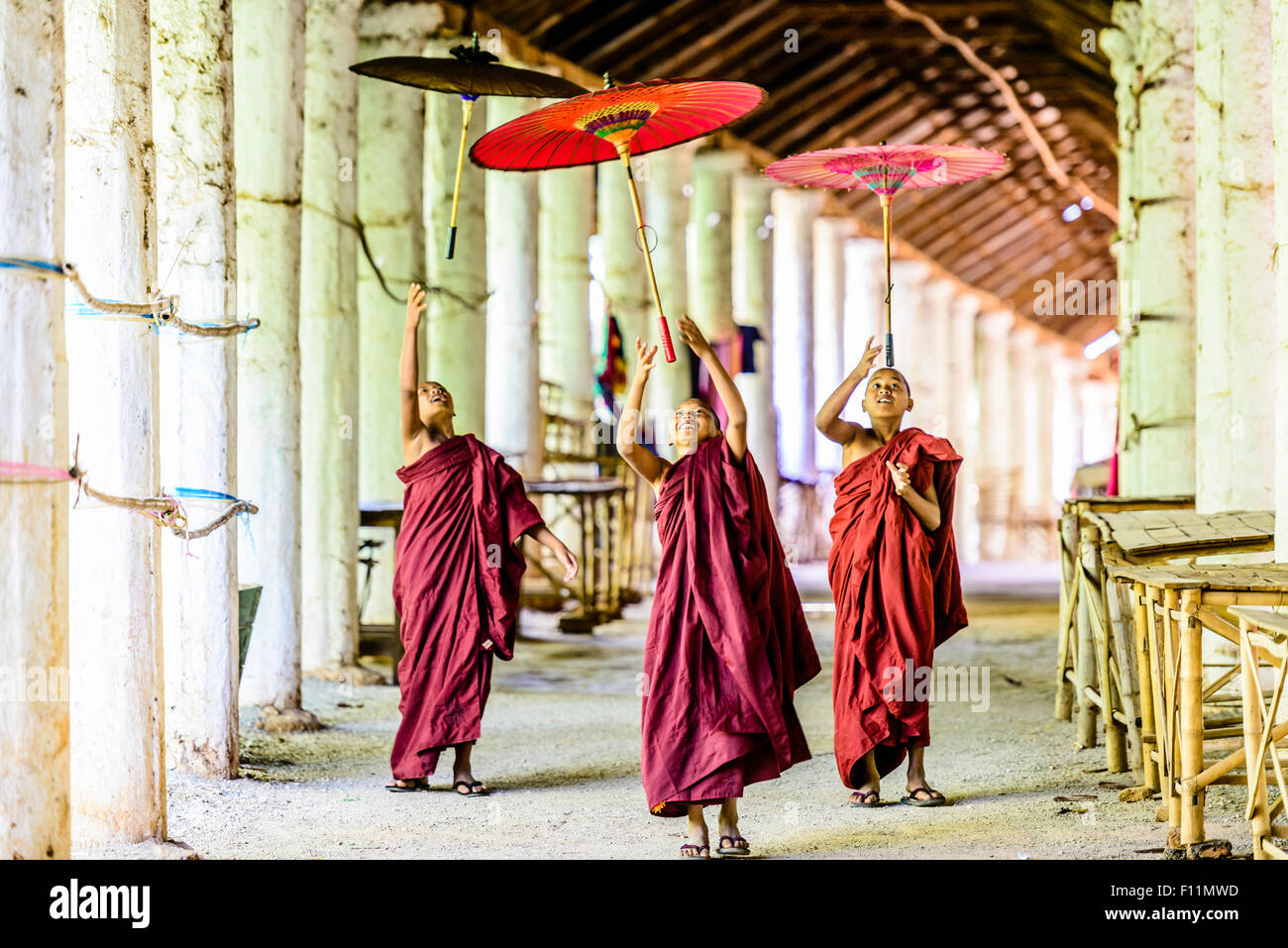 Asian monks-in-training playing with parasols in hallway Stock Photo