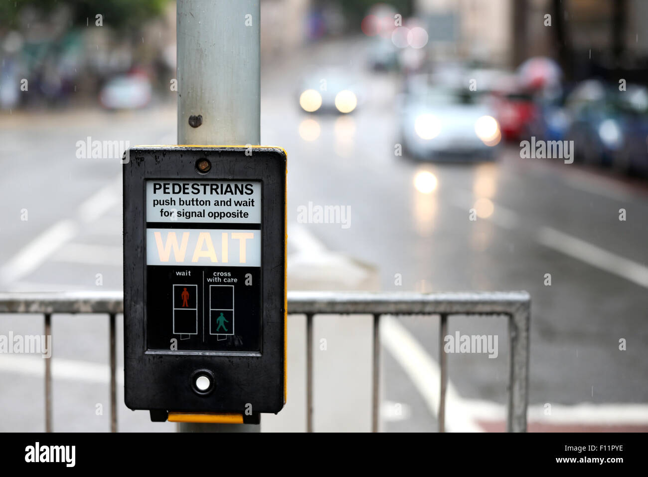 A traffic light pedestrian control on a busy city street. the illuminated street level pedestrian sign says WAIT as vehicles approach the crossing Stock Photo