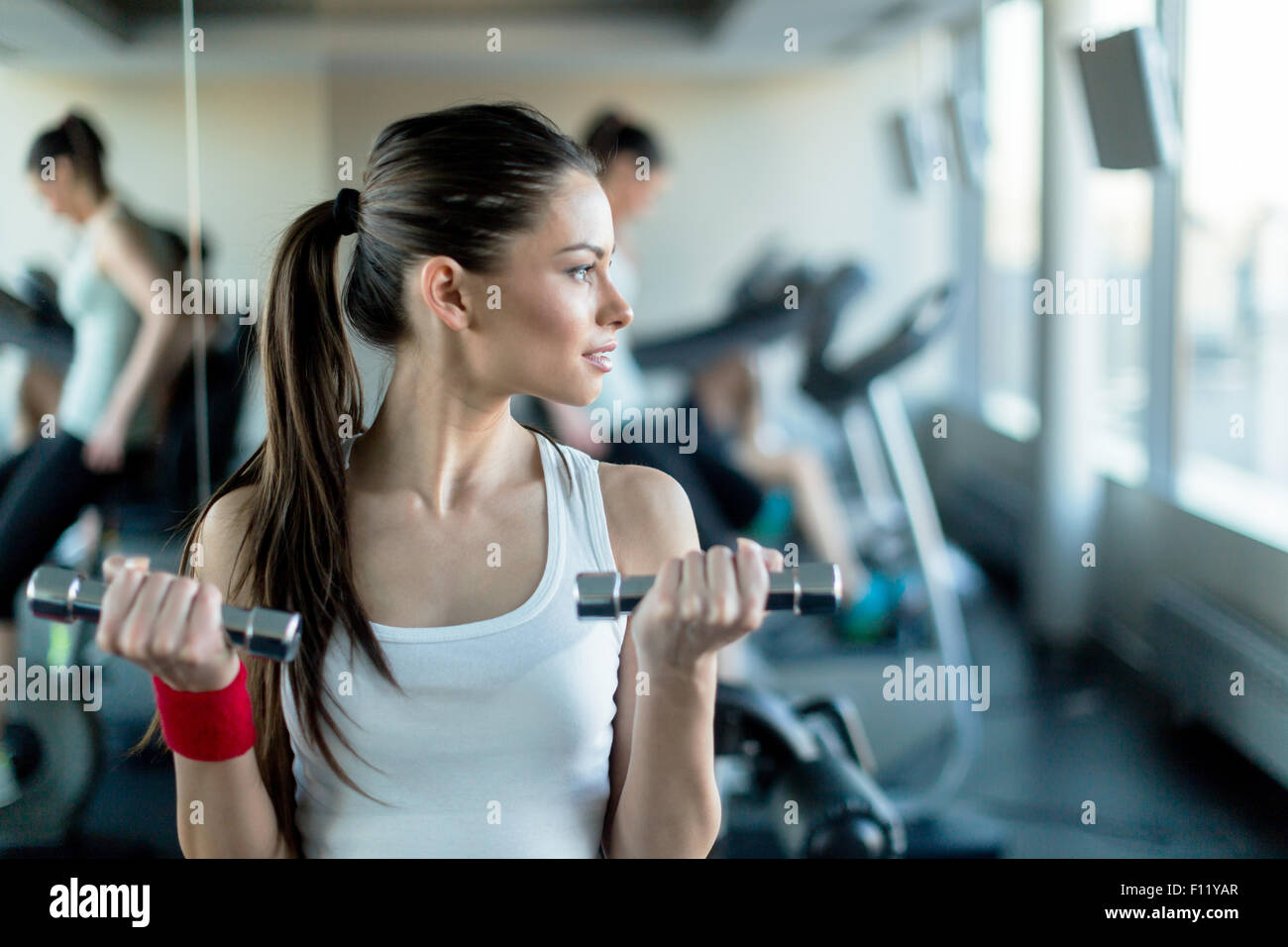 Beautiful, young woman lifting weights in a gym standing next to a mirror Stock Photo