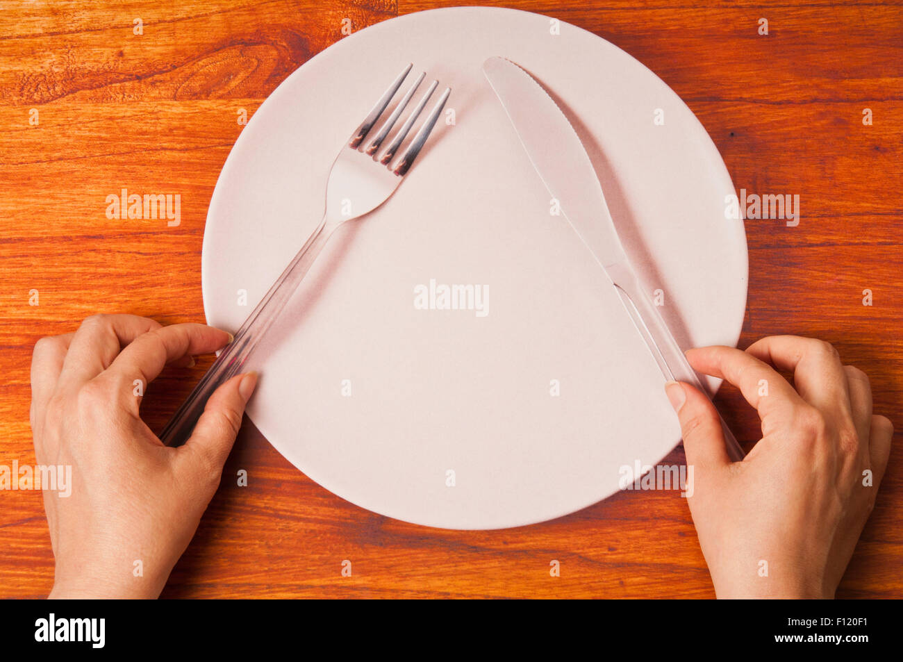 Trompe-l'œil of woman hands over a printed photo of a plate with fork and knife Stock Photo