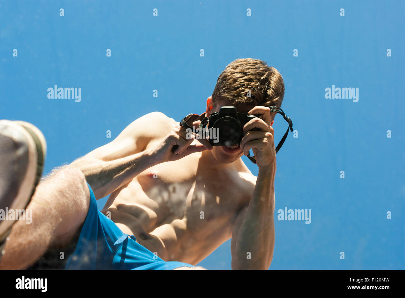 Lean but muscular man with his top off taking pictures of himself in a mirror.  Abstract shots.  The mirror is laying on grass. Stock Photo