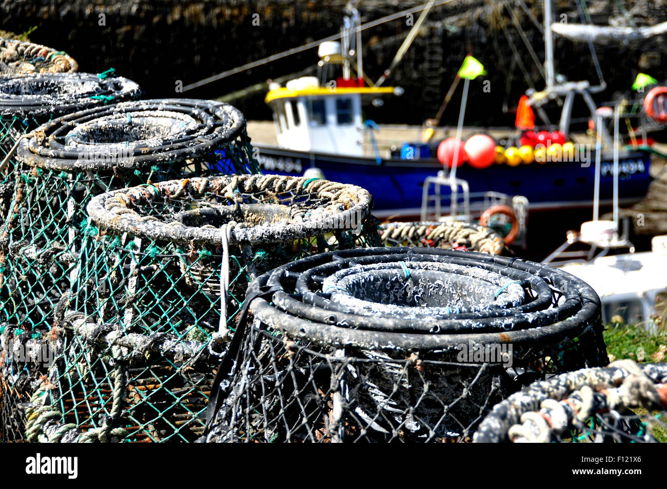 North Cornwall - Boscastle harbour - lobster pots on the quay - backdrop fishing boat - differential focus - bright sunlight Stock Photo
