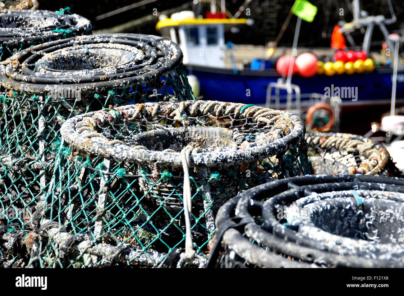 North Cornwall - Boscastle quay - lobster pots piled up - backdrop fishing boat - differential focus - bright sunlight Stock Photo