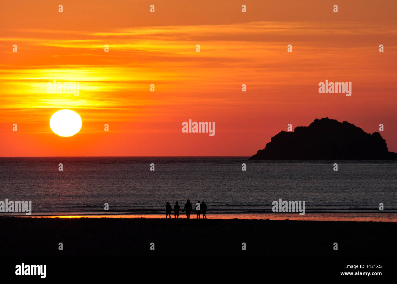 North Cornwall - sun setting over sea - beach figures in dark silhouette - off shore island outline - orange - red - gold sky Stock Photo