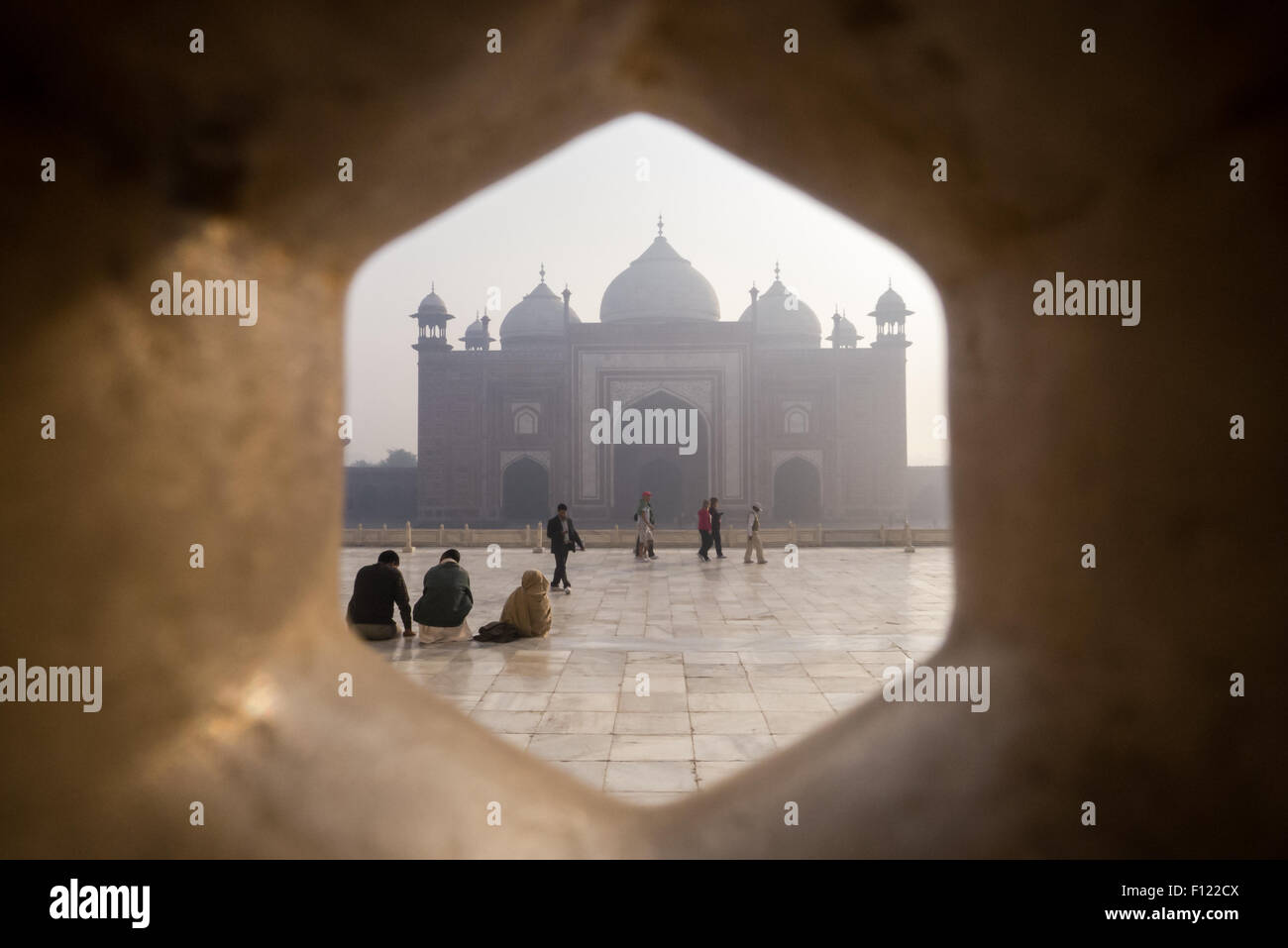 Agra, Uttar Pradesh, India. The Taj Mahal; main mausoleum; tourists and the Jawab building with its three domes outside seen through a lattice screen. Stock Photo