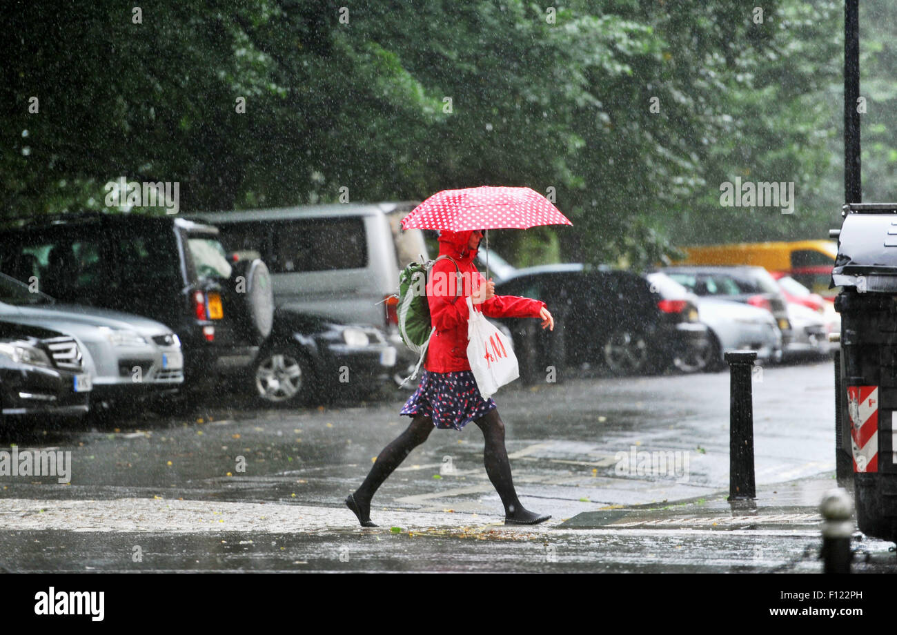 Brighton, UK. 25th August, 2015. A young woman with a red umbrella crosses the street as she gets caught in a torrential downpour of rain today in the centre of Brighton and Hove . Stock Photo