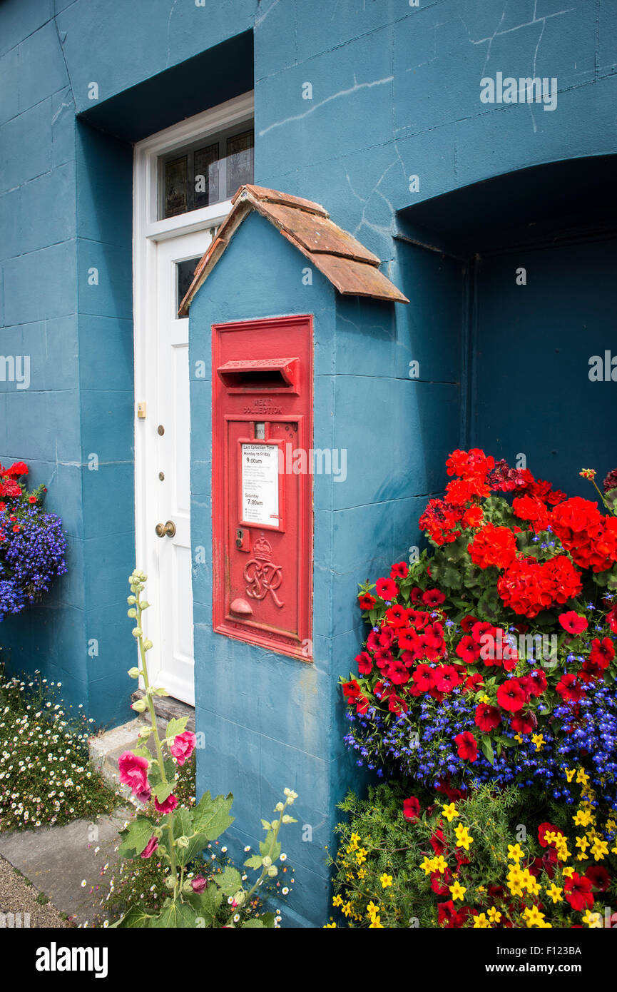 Red postbox built into the wall of a house with garden and flowers. Stock Photo