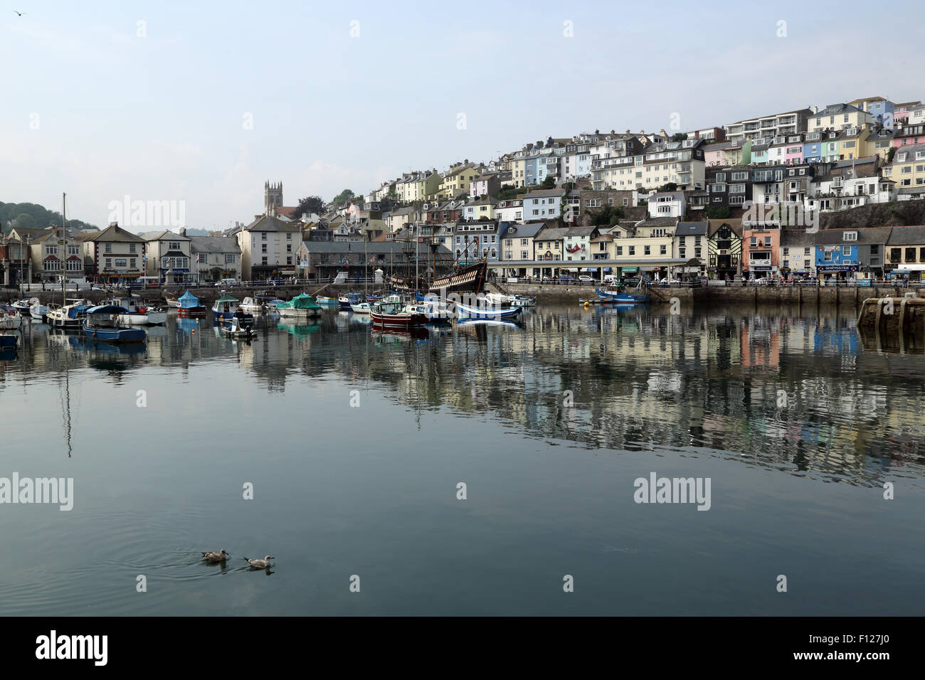 View of the harbour at Brixham, Devon, England, UK. Boats can be seen on the water, and houses, shops and restaurants behind. Stock Photo