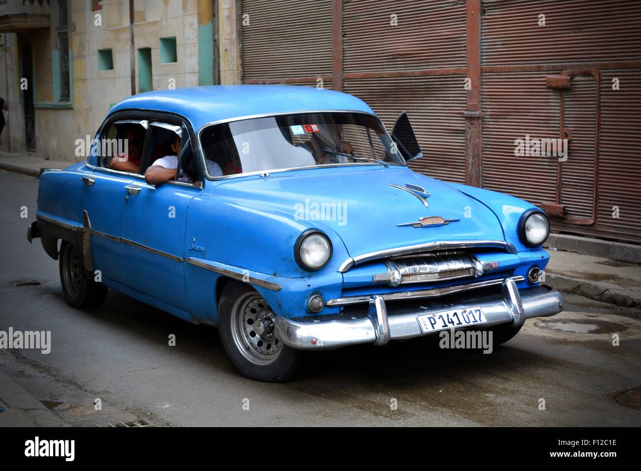 Vintage blue car with passengers driving down a wet street on the outskirts of Havana, Cuba Stock Photo