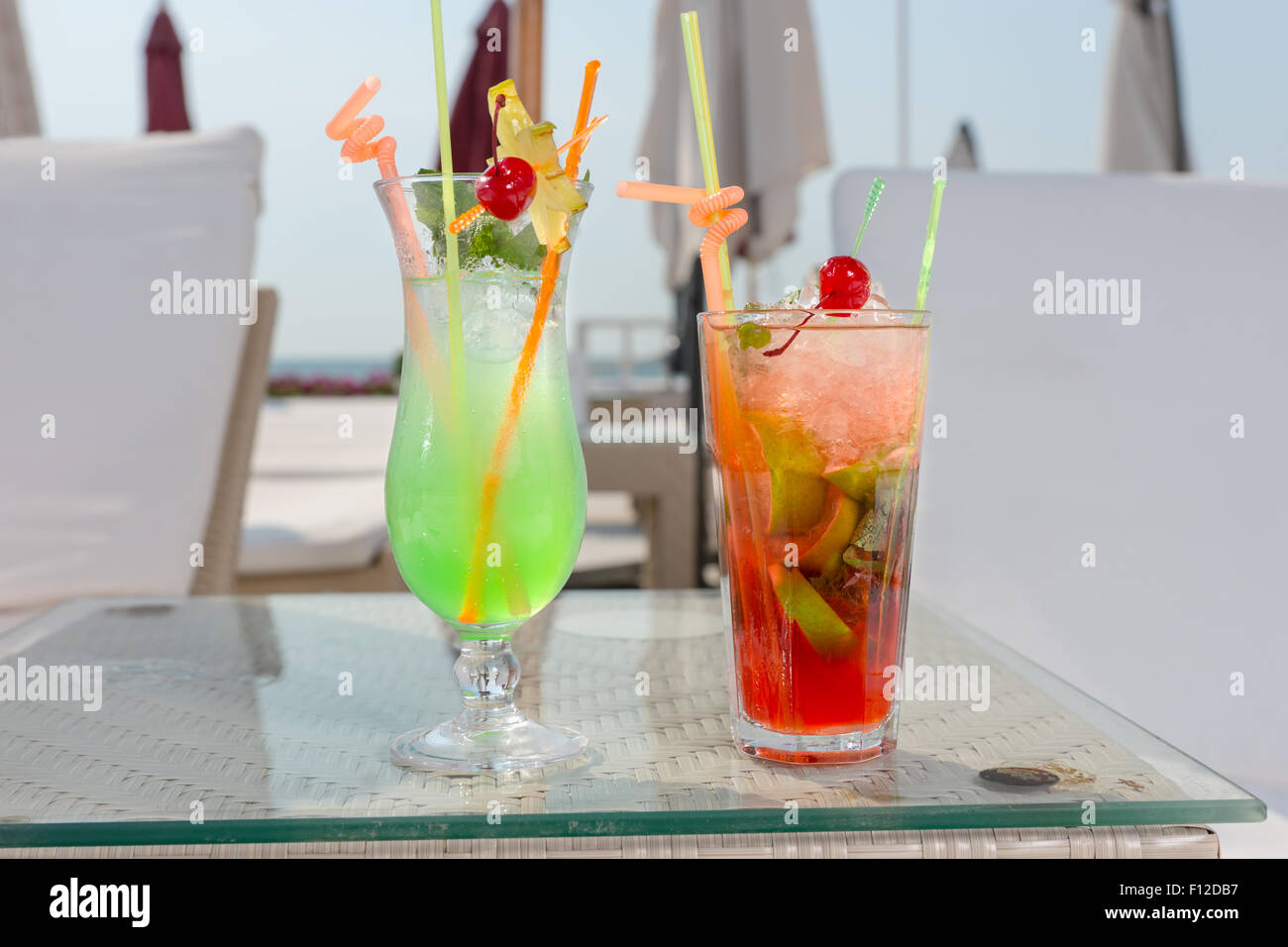 Two colorful tropical cocktails on ice standing side by side on a table amongst recliner chairs and umbrellas at a seaside resort on a summer vacation. Stock Photo