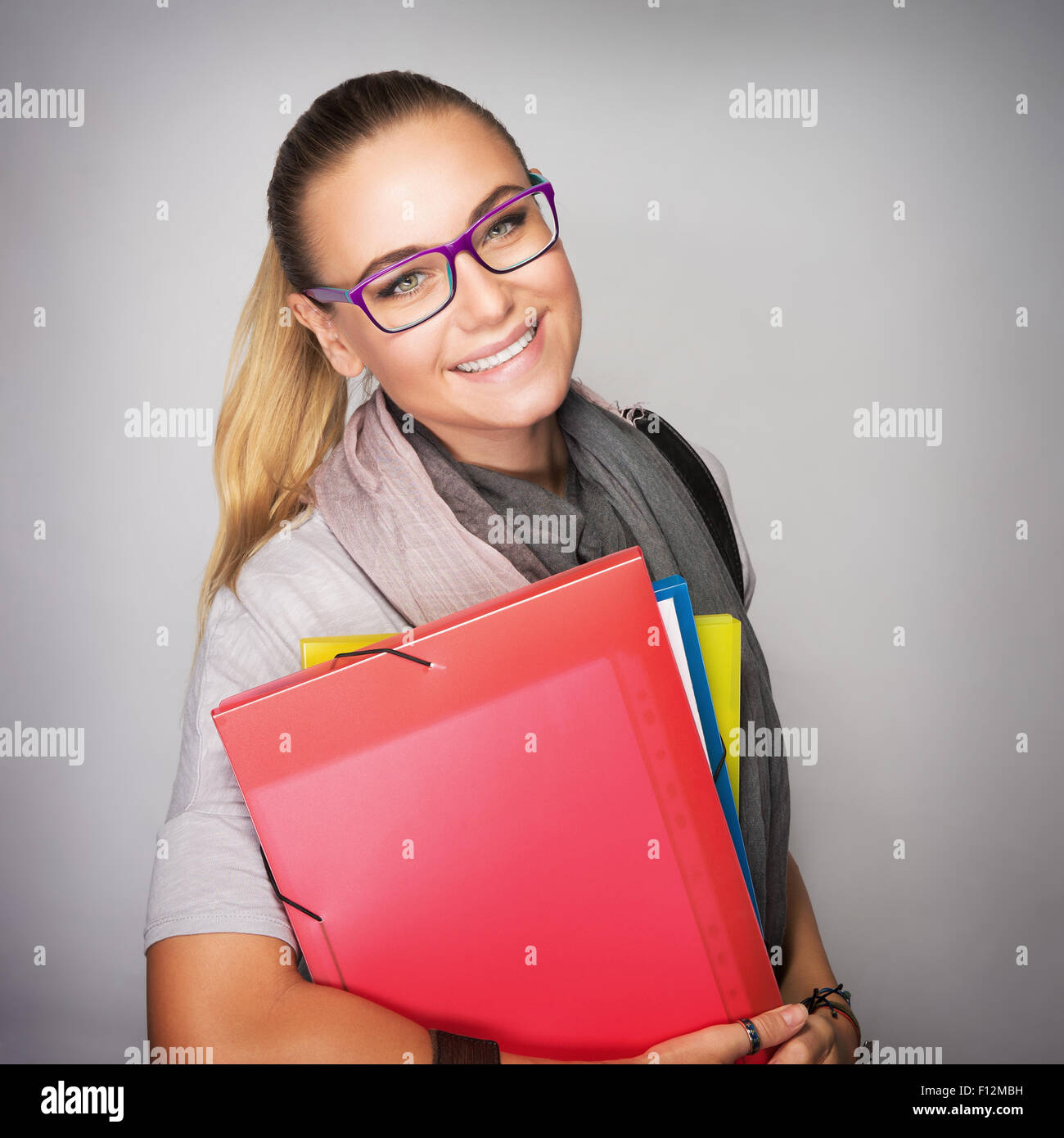 Happy student girl with colorful folders in hands isolated on gray background, enjoying start of school time, high education Stock Photo