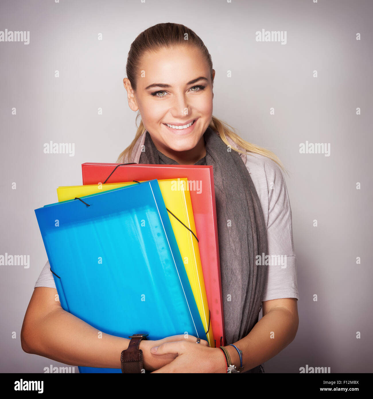 Portrait of beautiful happy student girl with colorful folders in hands over gray background, enjoying start of education Stock Photo