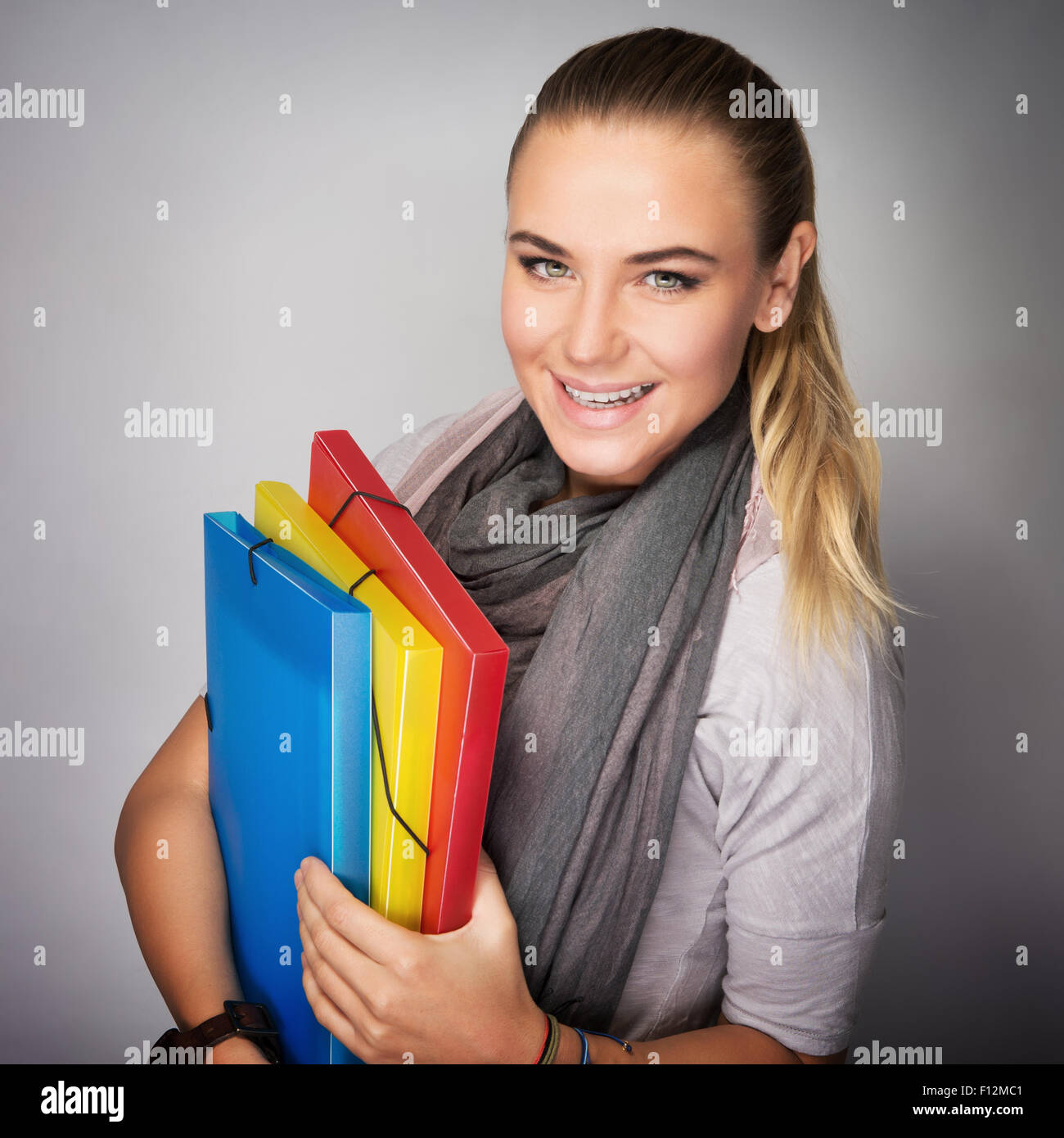 Portrait of beautiful happy student girl with colorful folders in hands over gray background, enjoying start of education Stock Photo