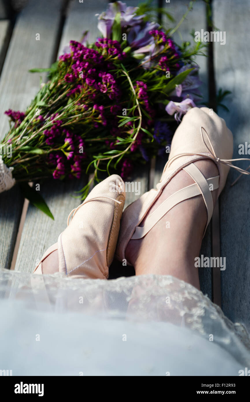 Woman's feet in ballet slippers with lace hem and a nearby bouquet of wildflowers. Stock Photo