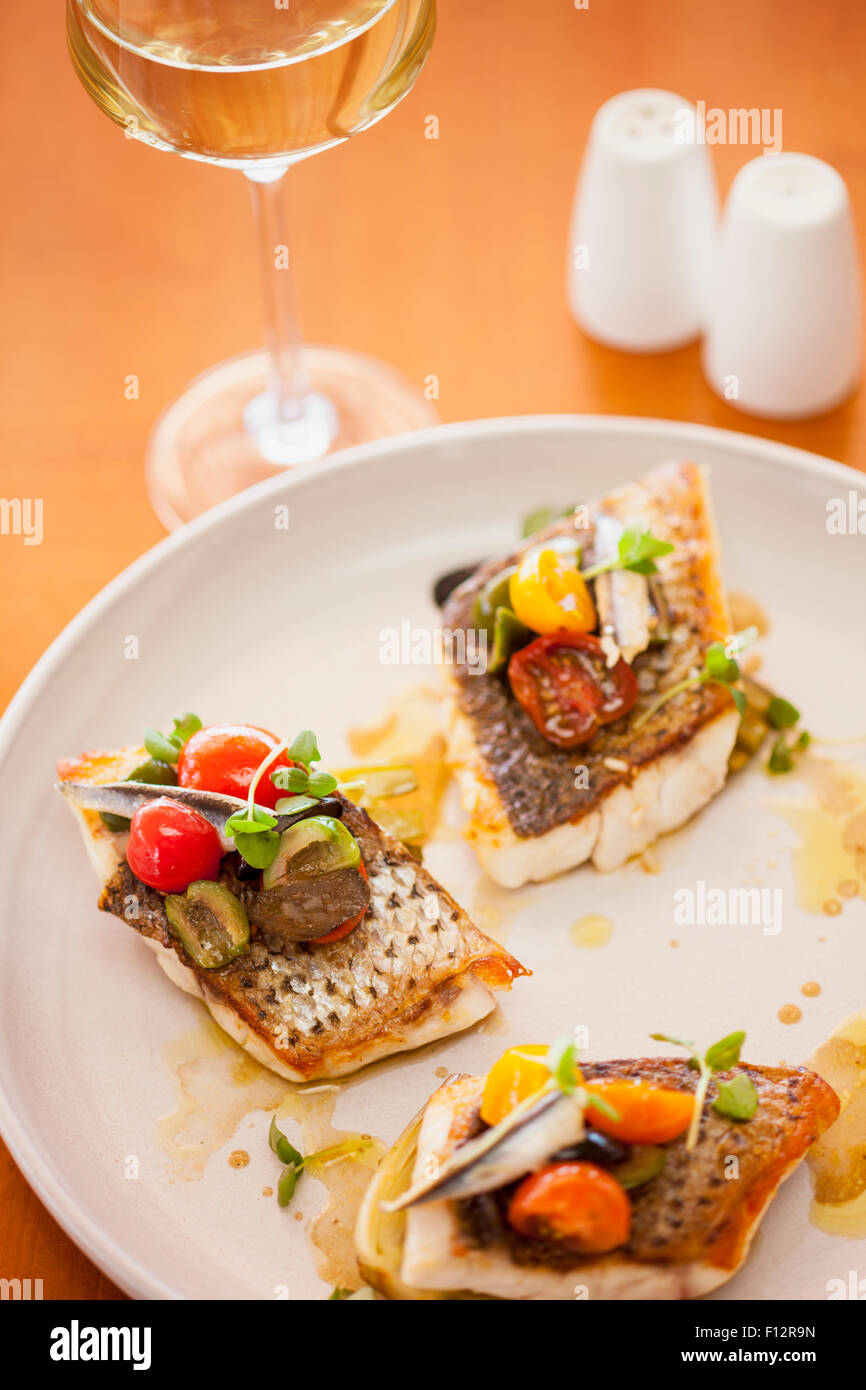 striped bass with cherry tomatoes, olives and anchovy with a glass of chardonnay, Tydes Restaurant, Coral Casino, Biltmore Hotel Stock Photo