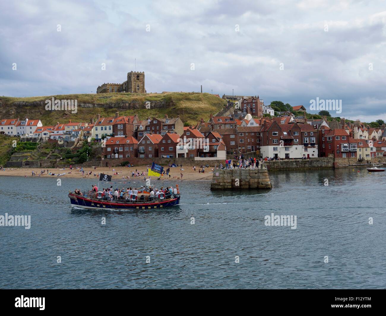 Church on a hill with a tourist boat in the foreground and a pier and village in the background Stock Photo