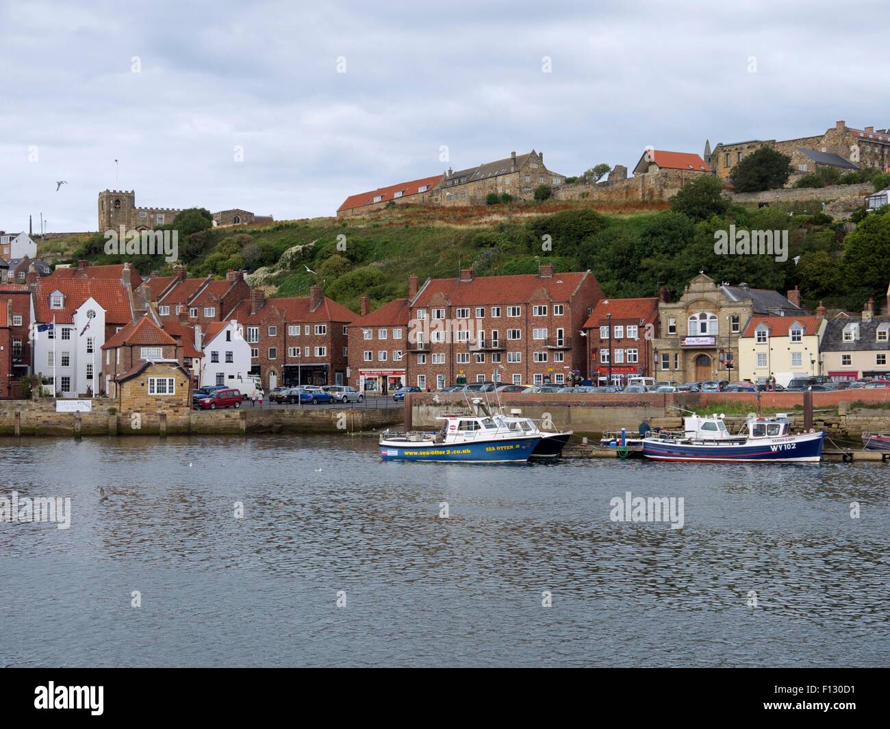 Fishing boats moored up in the harbor with houses and a church on the hill in the background Stock Photo