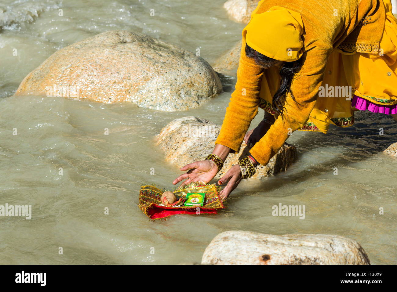 A female pilgrim at the banks of the river Ganges is praying, offering personal belongings to the holy water, Gangotri Stock Photo