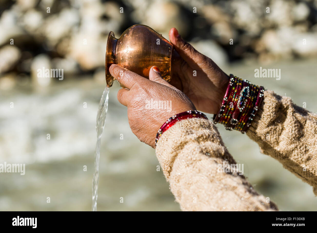 A female pilgrim praying, offering the holy water, at the banks of the river Ganges, Gangotri, Uttarakhand, India Stock Photo
