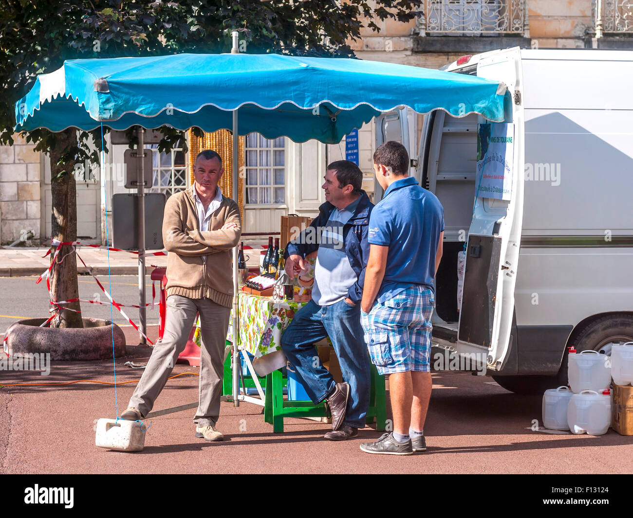 Three men chatting at outdoor market wine stand - France. Stock Photo