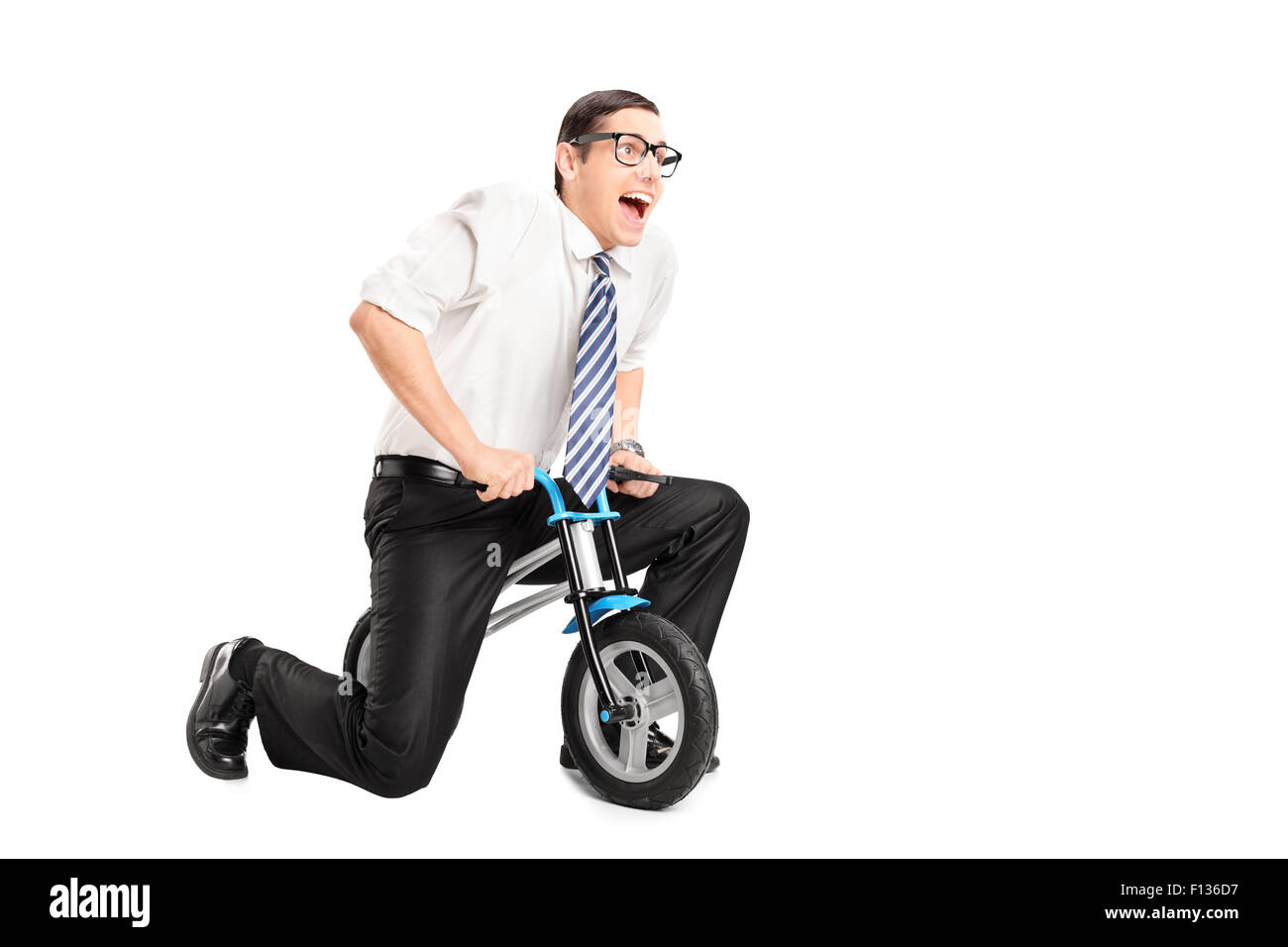Silly young businessman riding a small bike and looking forward isolated on white background Stock Photo