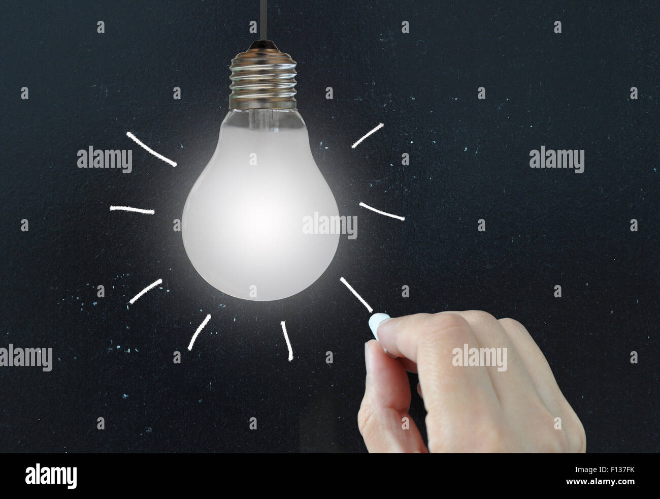 Hand drawing light rays around a hanging bulb against a blackboard ...