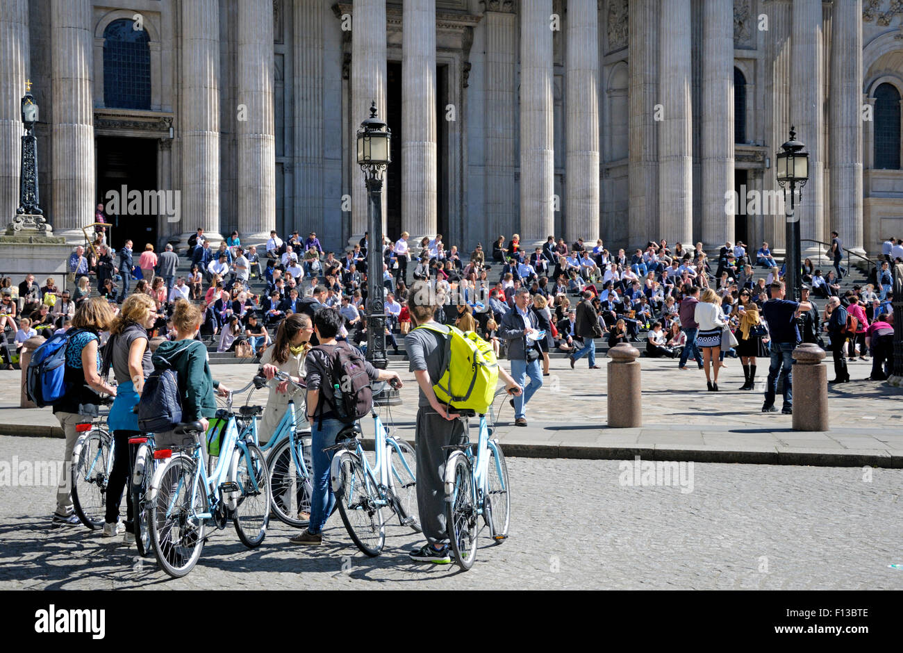 London, England, UK. People sitting in the sun on the steps of St Paul's Cathedral - group of cyclists Stock Photo