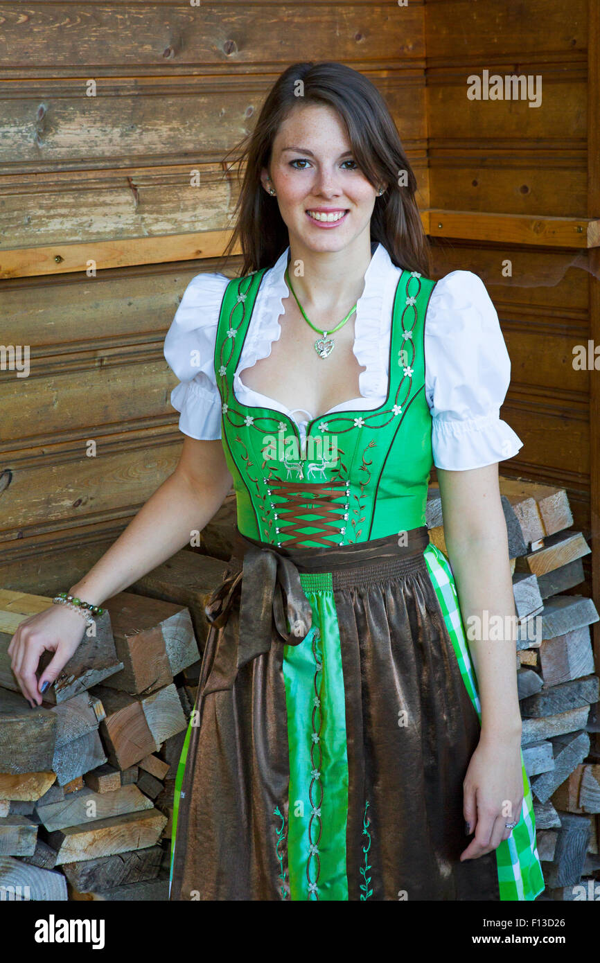 young woman wearing bavarian dirndl and standing in front of stack of wood Stock Photo