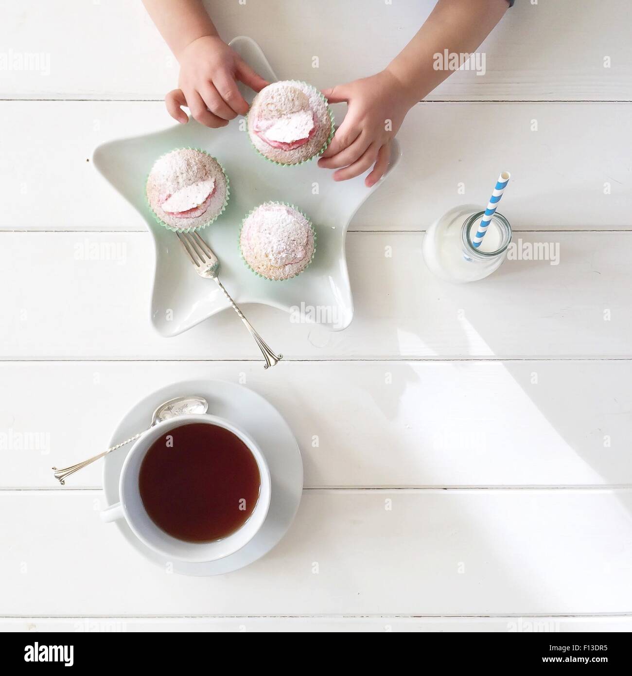 Boy's hands taking a cupcake, with tea and bottle of milk Stock Photo