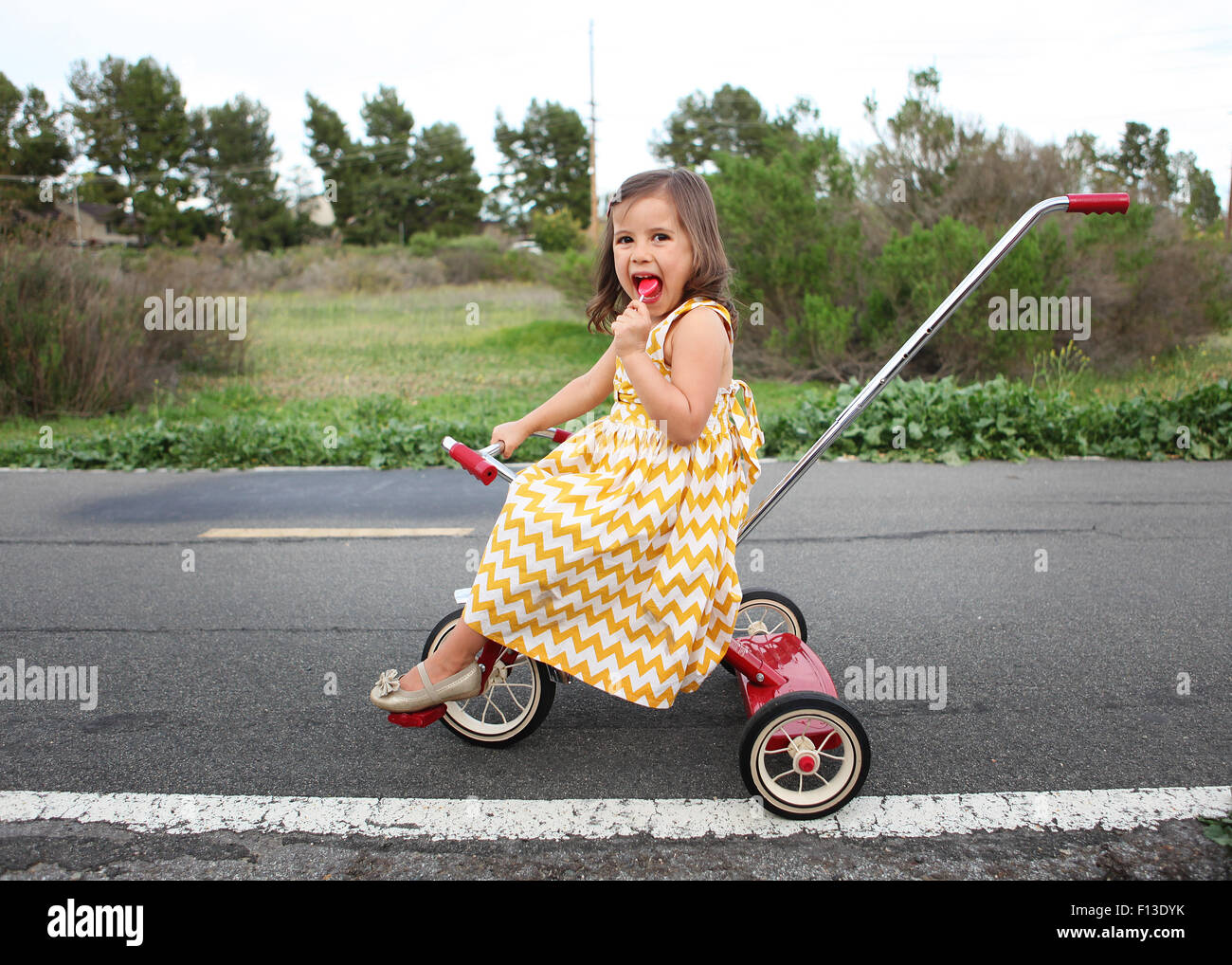 Girl on tricycle eating lollipop Stock Photo