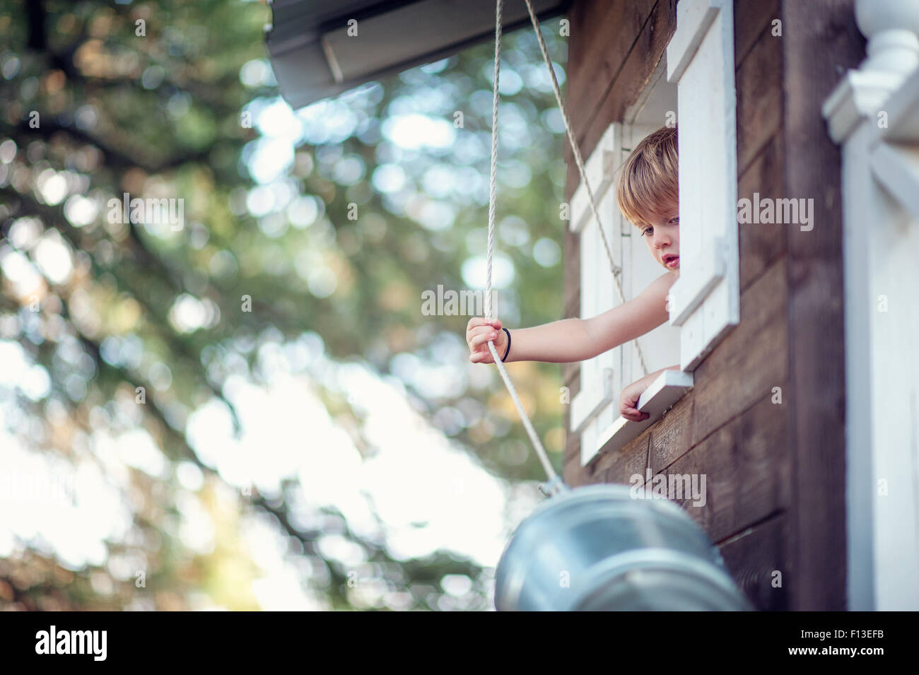 Boy pulling a bucket up to his treehouse Stock Photo