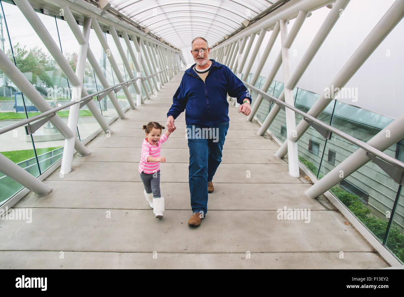 Girl and her grandfather holding hands, walking across a walkway Stock Photo