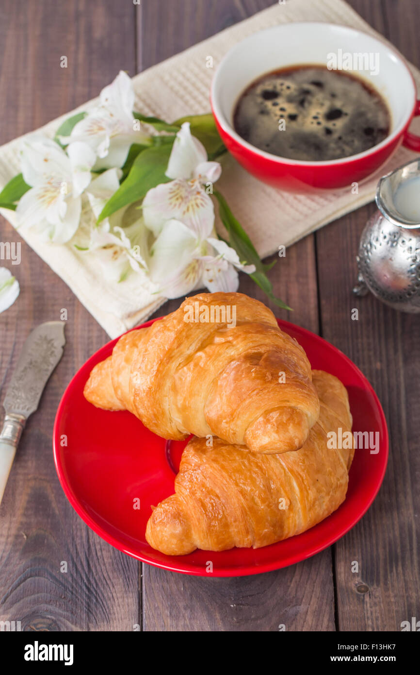 Fresh baked croissants with and coffee and cream on wooden background