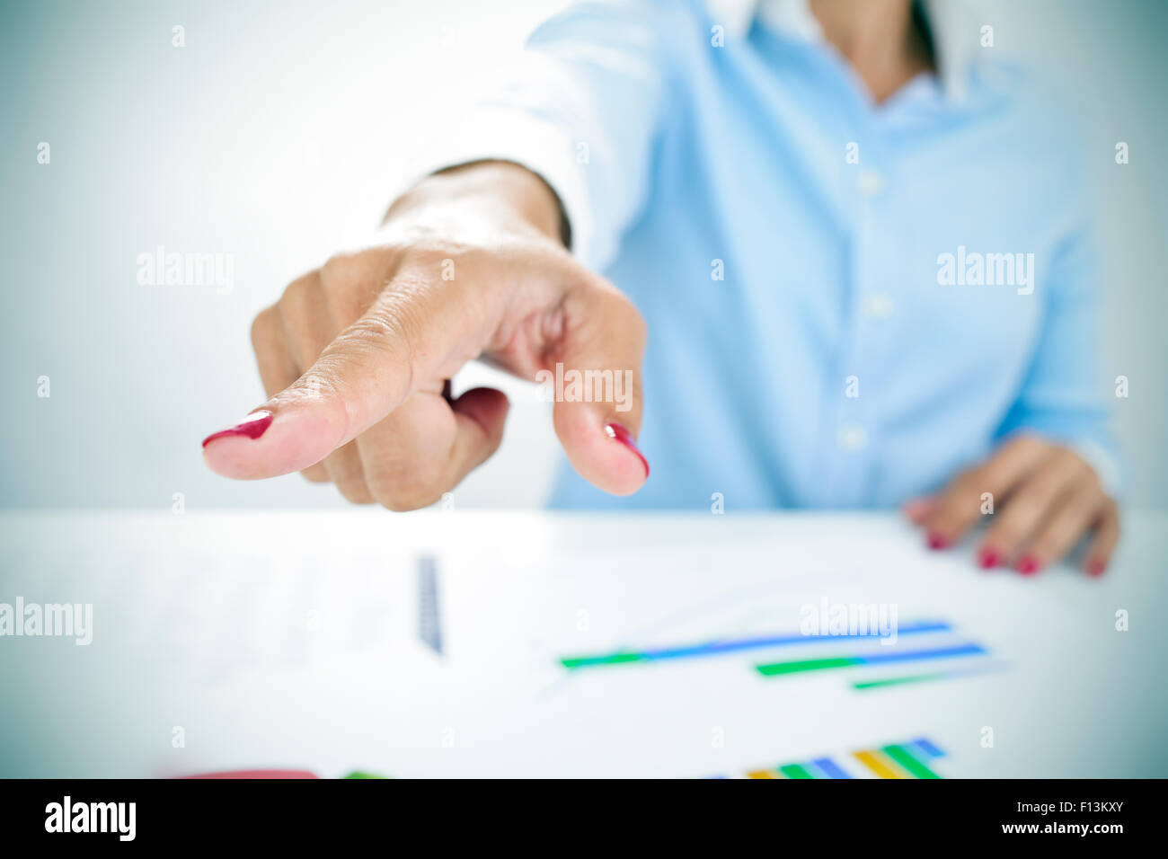 closeup of a businesswoman sitting at her desk, full of charts, pointing with her finger the way out Stock Photo
