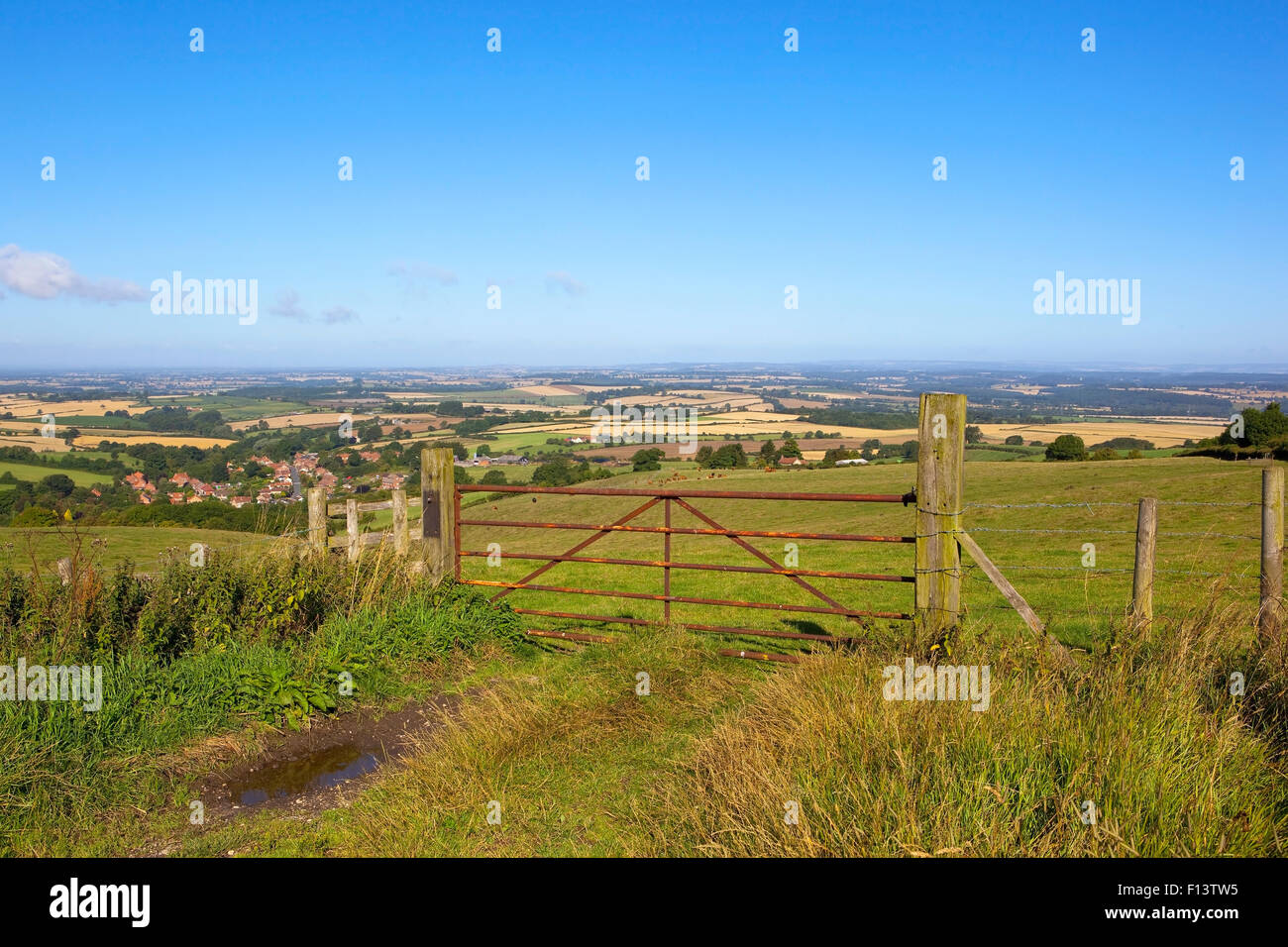 Acklam village and the distant vale of York viewed over a metal five bar gate high on the Yorkshire wolds in August. Stock Photo