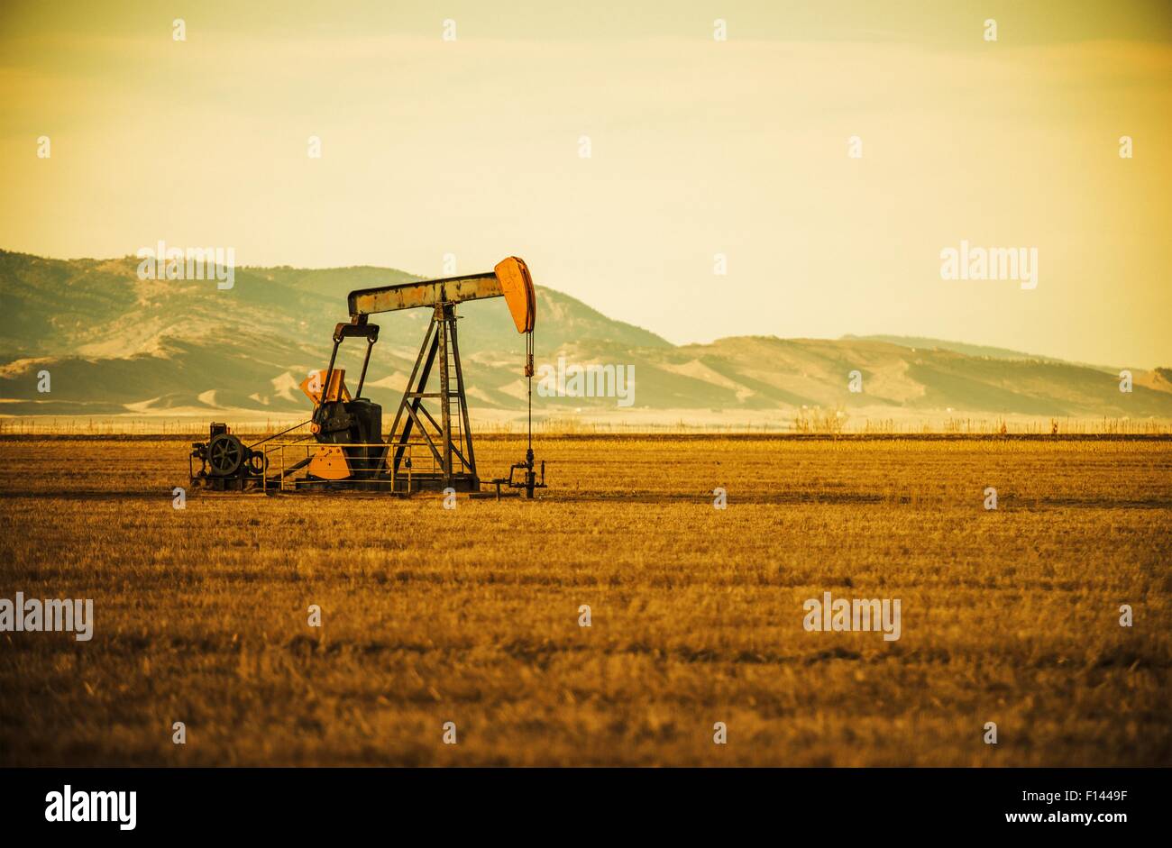 Aged Oil Pump on Colorado Prairie with Mountain Hills in the Background. Oil Industry Theme. Stock Photo
