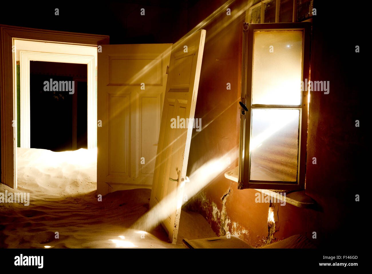 Light streaming through window on sand covered house in Kolmanskop Ghost Town, an old diamond-mining town where shifting sand dunes have encroached abandoned houses, Namib Desert Namibia, October 2013. Stock Photo