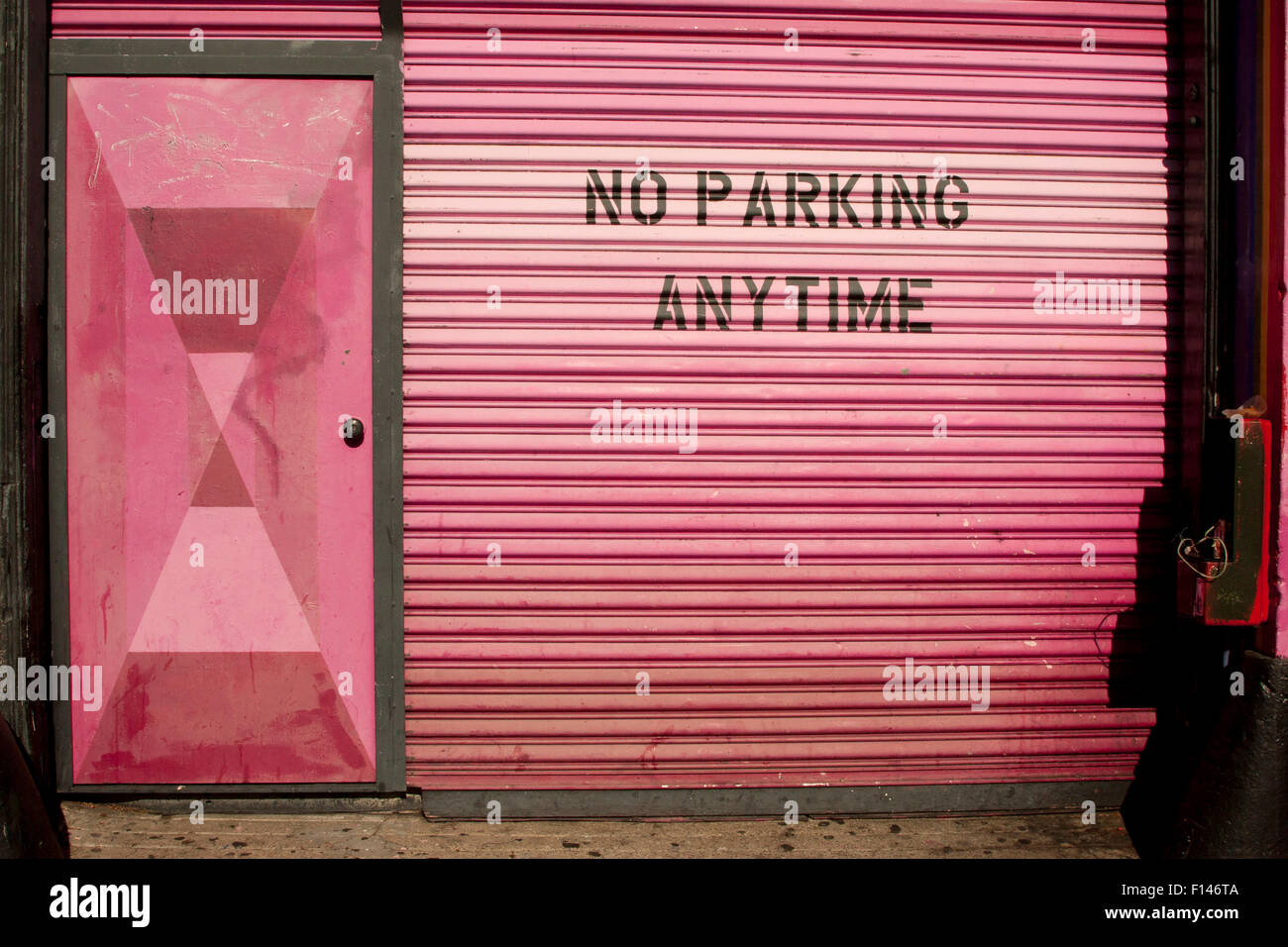 Pink roll-up garage door with the ever present 'NO PARKING ANYTIME' sign on Valencia Street, in The Mission in San Francisco. Stock Photo